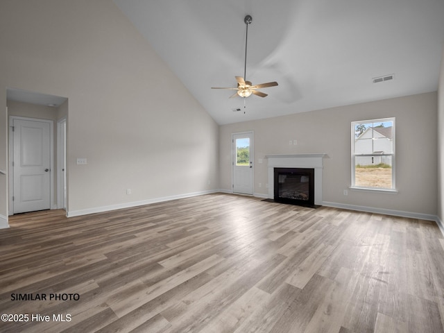 unfurnished living room with wood finished floors, baseboards, visible vents, high vaulted ceiling, and a fireplace with flush hearth