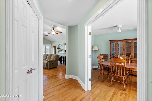 hallway featuring baseboards, light wood-style floors, and lofted ceiling