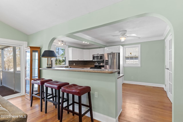 kitchen featuring a breakfast bar area, light wood-type flooring, arched walkways, white cabinets, and stainless steel appliances