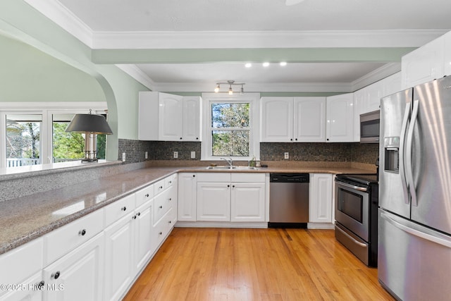 kitchen with light wood finished floors, a sink, ornamental molding, stainless steel appliances, and white cabinetry