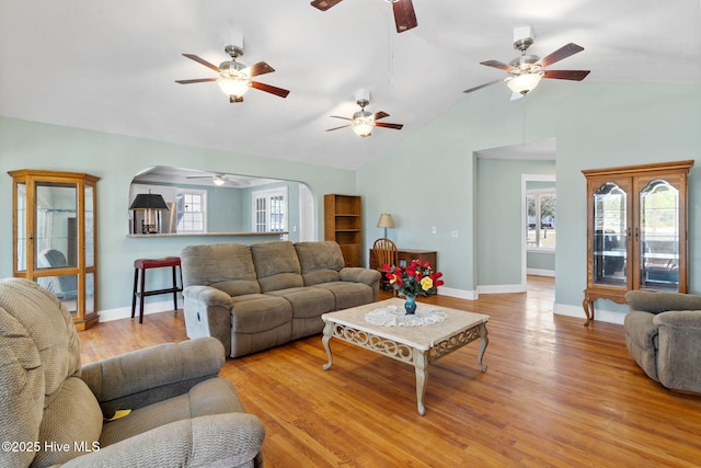 living area featuring baseboards, arched walkways, ceiling fan, and light wood finished floors