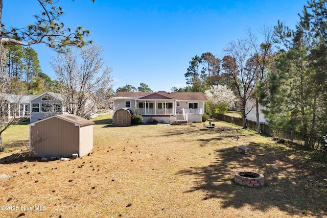 rear view of house with a shed, a fire pit, an outdoor structure, and fence