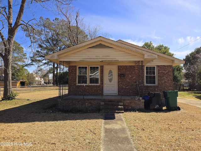 bungalow-style house with a porch, fence, brick siding, and a front lawn