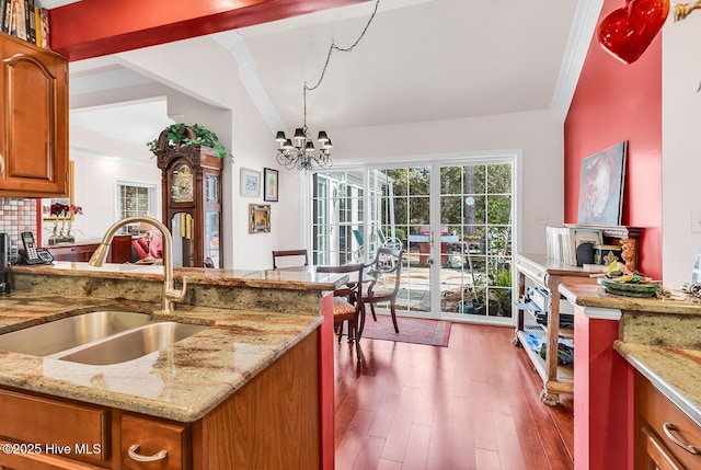 kitchen with light stone counters, wood finished floors, brown cabinetry, a sink, and a chandelier