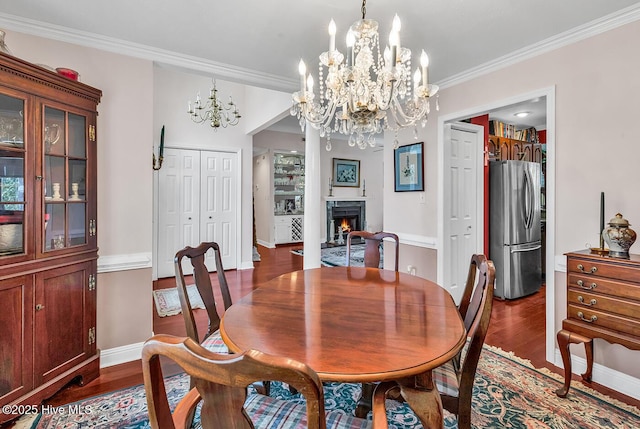 dining area with a warm lit fireplace, dark wood-type flooring, an inviting chandelier, and crown molding