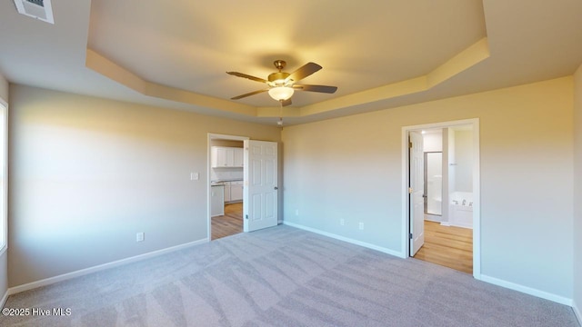 unfurnished bedroom with a tray ceiling, carpet flooring, baseboards, and visible vents