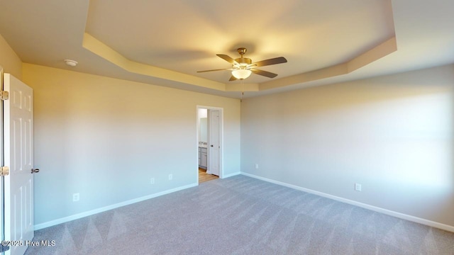 empty room with light colored carpet, a raised ceiling, baseboards, and ceiling fan