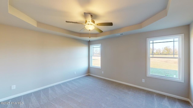 carpeted spare room with visible vents, ceiling fan, baseboards, and a tray ceiling