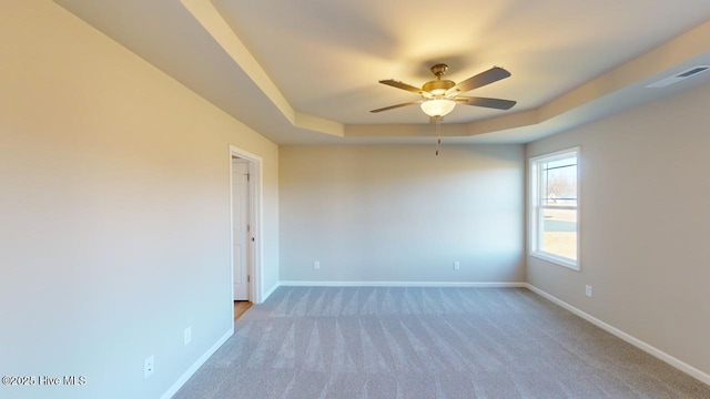 empty room featuring a tray ceiling, light colored carpet, baseboards, and visible vents