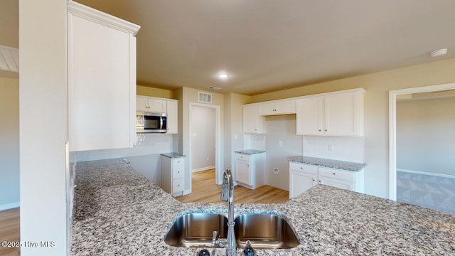 kitchen featuring visible vents, a sink, stainless steel microwave, tasteful backsplash, and light stone countertops