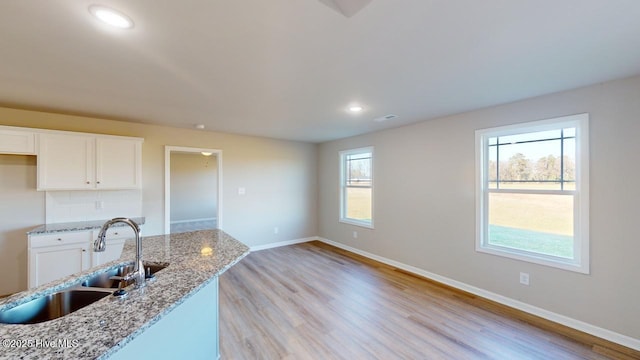 kitchen featuring white cabinetry, light stone countertops, baseboards, and a sink