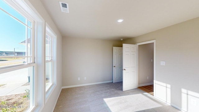 unfurnished room featuring light colored carpet, baseboards, visible vents, and a wealth of natural light