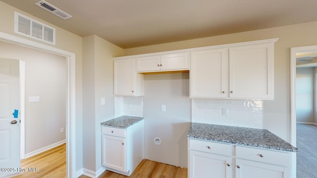 kitchen with white cabinets, visible vents, and stone counters