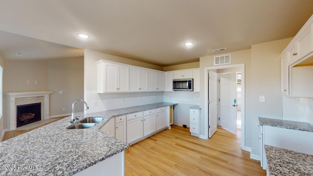 kitchen featuring stainless steel microwave, light stone countertops, light wood-style floors, and a sink