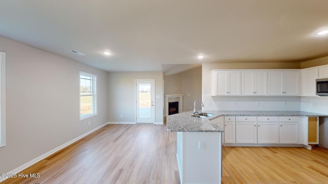 kitchen with a sink, stainless steel microwave, a peninsula, white cabinets, and a fireplace