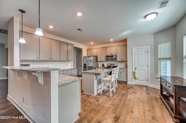 kitchen with stainless steel appliances, a kitchen breakfast bar, visible vents, and light wood-style flooring