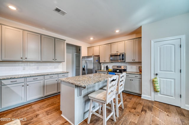 kitchen featuring visible vents, gray cabinetry, wood finished floors, stainless steel appliances, and a breakfast bar area