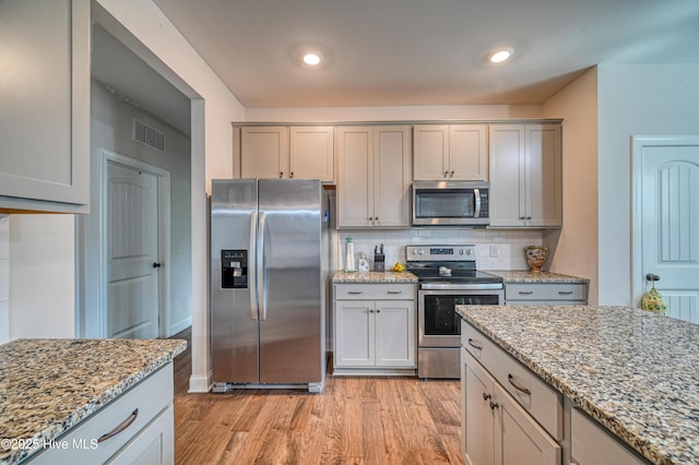 kitchen featuring light stone countertops, tasteful backsplash, appliances with stainless steel finishes, and light wood-style flooring