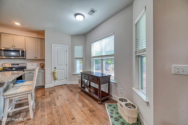 kitchen featuring visible vents, light wood-style flooring, light stone counters, tasteful backsplash, and stainless steel appliances