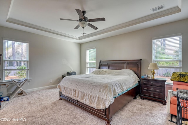 bedroom with visible vents, light colored carpet, a tray ceiling, and multiple windows