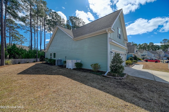 view of side of home featuring board and batten siding, an attached garage, fence, central AC, and driveway