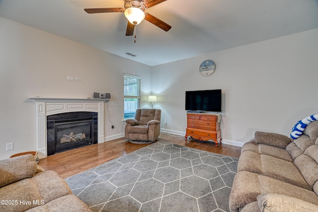 living room with visible vents, baseboards, wood finished floors, a glass covered fireplace, and a ceiling fan