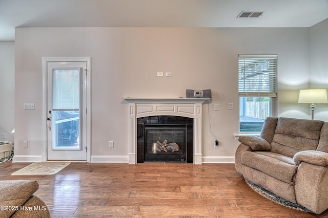 living room featuring a tiled fireplace, wood finished floors, visible vents, and baseboards