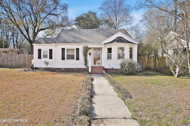 view of front facade with a front lawn, fence, and roof with shingles