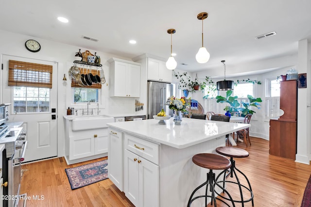 kitchen featuring visible vents, light wood-type flooring, high end refrigerator, a kitchen breakfast bar, and a sink