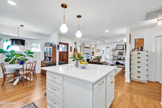 kitchen with visible vents, a kitchen island, light wood-style floors, and white cabinetry