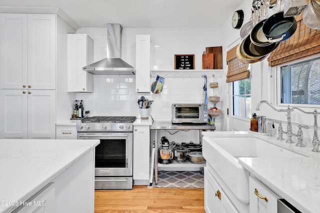 kitchen featuring backsplash, stainless steel range with gas stovetop, white cabinets, wall chimney exhaust hood, and a sink