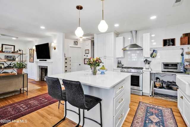 kitchen featuring visible vents, wall chimney range hood, open floor plan, light wood finished floors, and stainless steel gas range