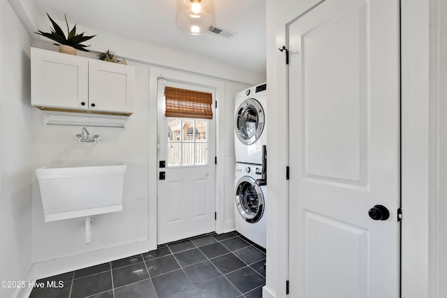 clothes washing area with visible vents, laundry area, a sink, stacked washer and clothes dryer, and dark tile patterned floors