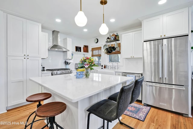 kitchen with a breakfast bar, freestanding refrigerator, white cabinets, wall chimney range hood, and gas range