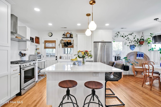 kitchen with a kitchen island, appliances with stainless steel finishes, a kitchen breakfast bar, light wood-style floors, and wall chimney exhaust hood