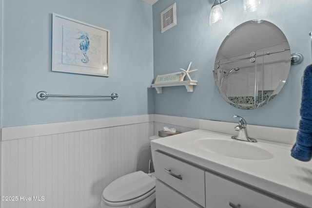 full bathroom with a wainscoted wall, visible vents, toilet, a shower, and vanity