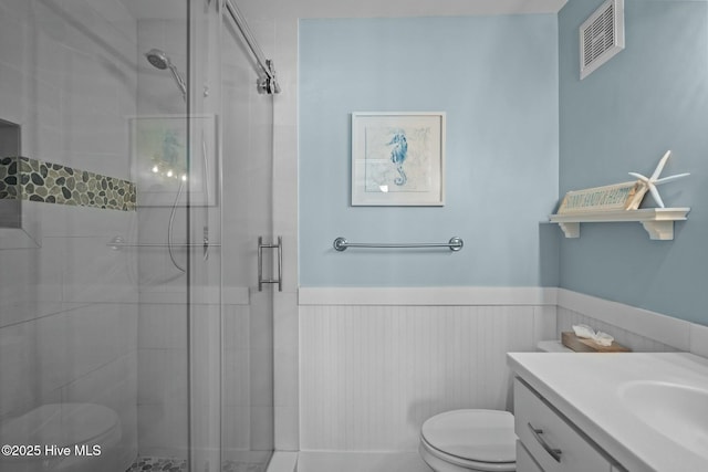 bathroom featuring visible vents, a wainscoted wall, toilet, a stall shower, and vanity