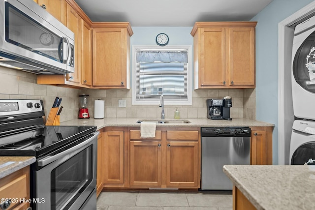 kitchen with stacked washer / dryer, light tile patterned floors, decorative backsplash, stainless steel appliances, and a sink