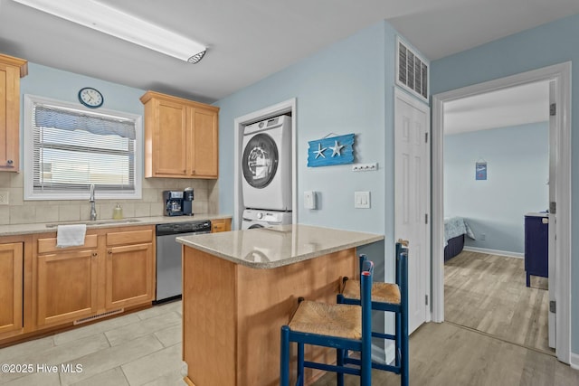 kitchen featuring visible vents, stacked washing maching and dryer, a sink, dishwasher, and tasteful backsplash