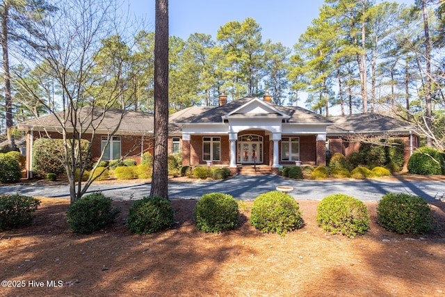 view of front of home featuring brick siding, curved driveway, and a chimney