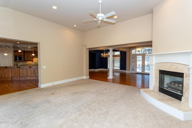 unfurnished living room featuring high vaulted ceiling, a high end fireplace, recessed lighting, carpet flooring, and ornate columns