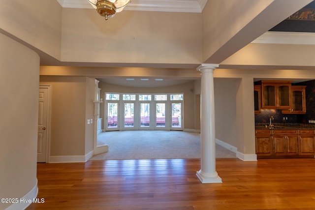 entryway with crown molding, baseboards, light wood-type flooring, a towering ceiling, and ornate columns