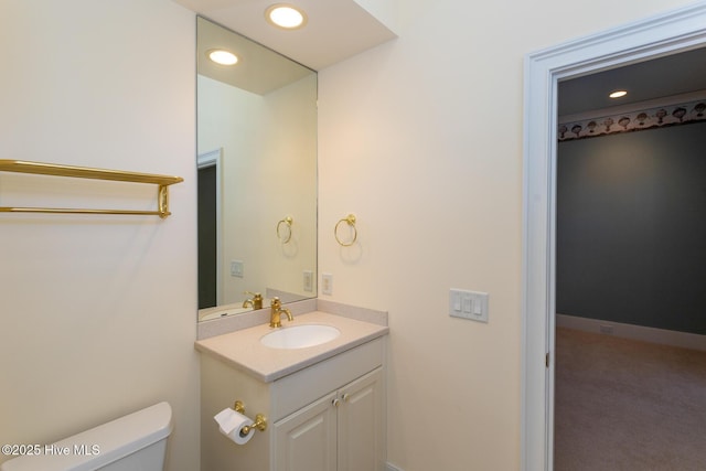 half bathroom with vanity, toilet, recessed lighting, and baseboards