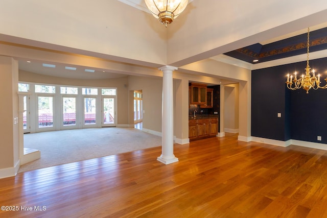 interior space with baseboards, light wood finished floors, ornate columns, a high ceiling, and a chandelier