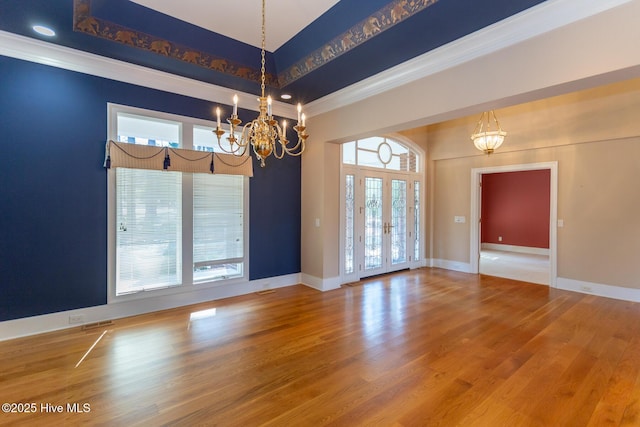 empty room with a tray ceiling, wood finished floors, baseboards, and a chandelier