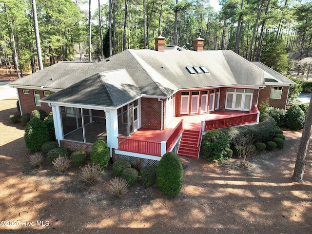 rear view of property featuring brick siding, a shingled roof, a wooden deck, a chimney, and a sunroom