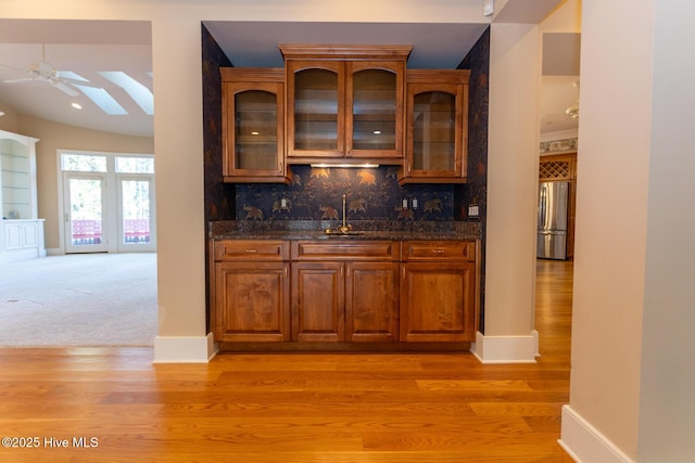 bar featuring tasteful backsplash, light wood-style flooring, freestanding refrigerator, and a sink