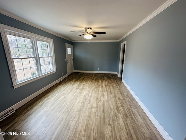 spare room with wood finished floors, visible vents, baseboards, and ornamental molding