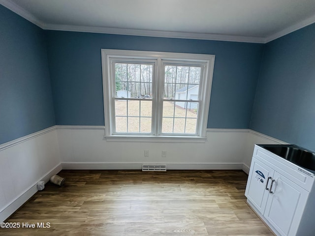 unfurnished room featuring visible vents, a wainscoted wall, ornamental molding, and light wood finished floors