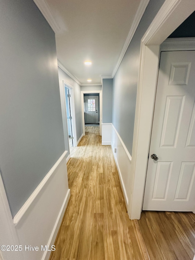 corridor featuring a wainscoted wall, baseboards, light wood-type flooring, and ornamental molding